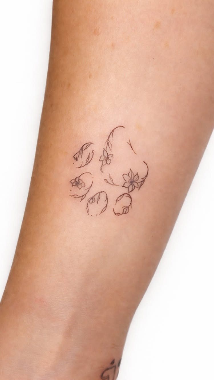 Floral paw print tattoo with delicate line work on a person's forearm