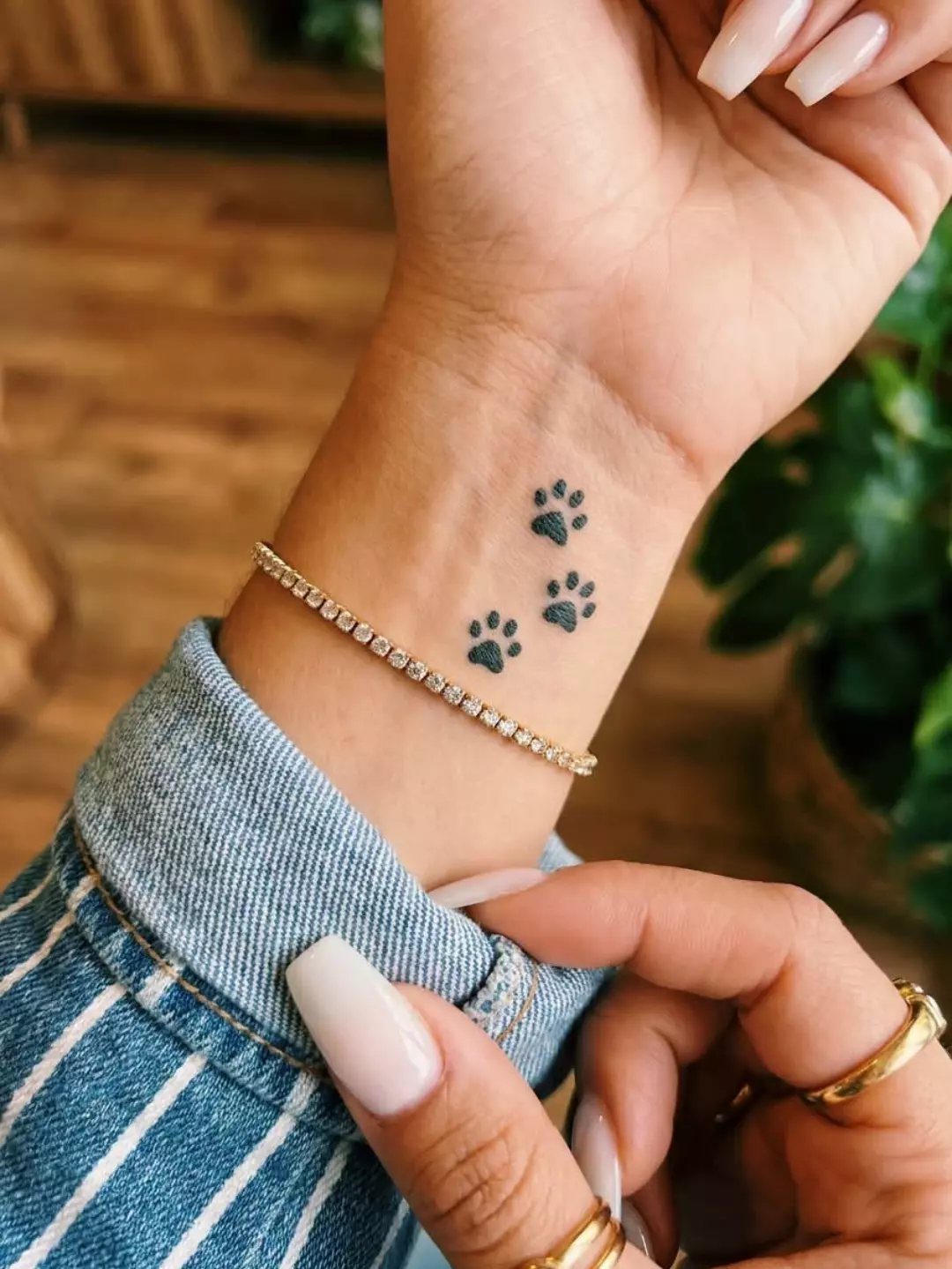 Three small black paw print tattoos on a person's wrist with a diamond bracelet.