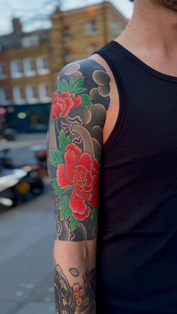 Japanese sleeve tattoo with red peony flowers and grey clouds on an arm