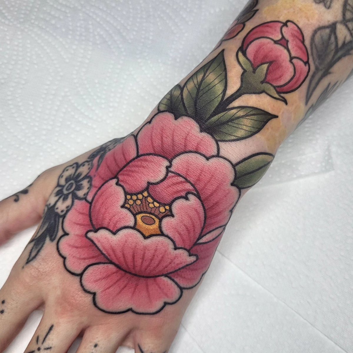 Pink peony bloom and bud tattoo on a person's foot and ankle.