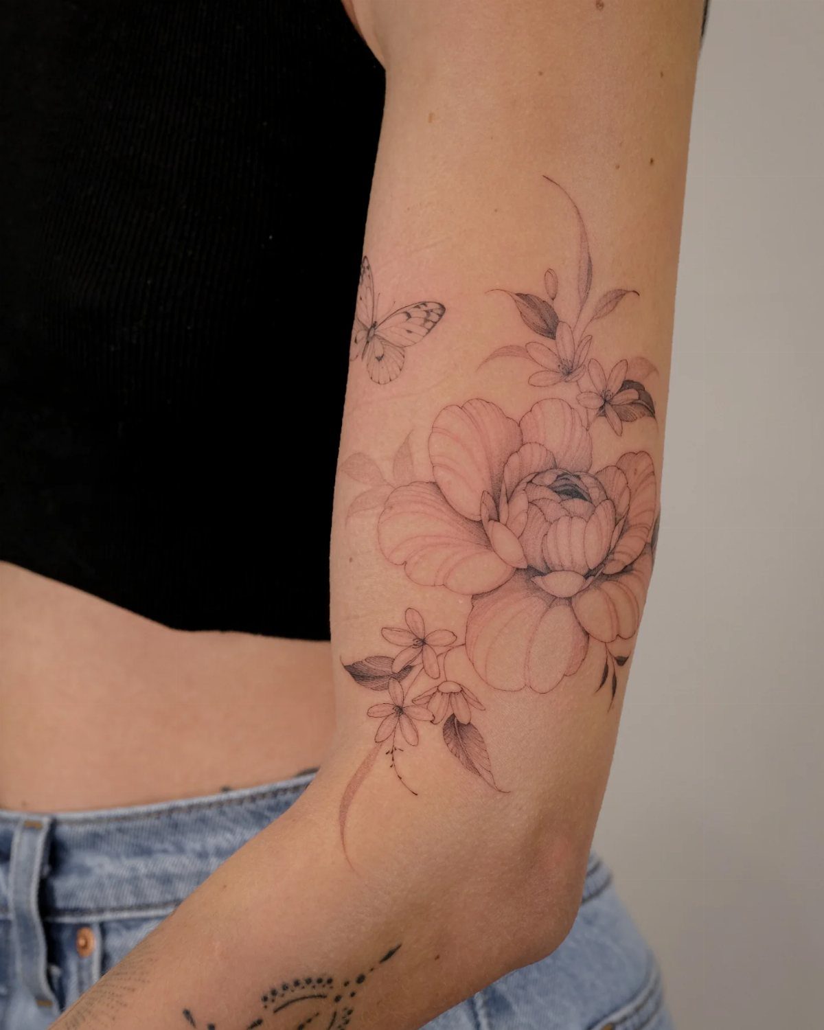Fine-line tattoo of a pink peony flower and a butterfly on a forearm.