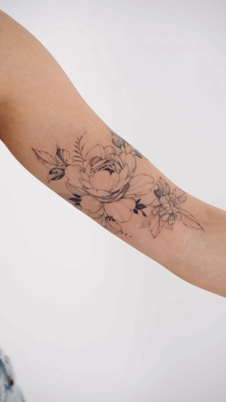 Peony flower linework tattoo on a person's forearm with black ink details.