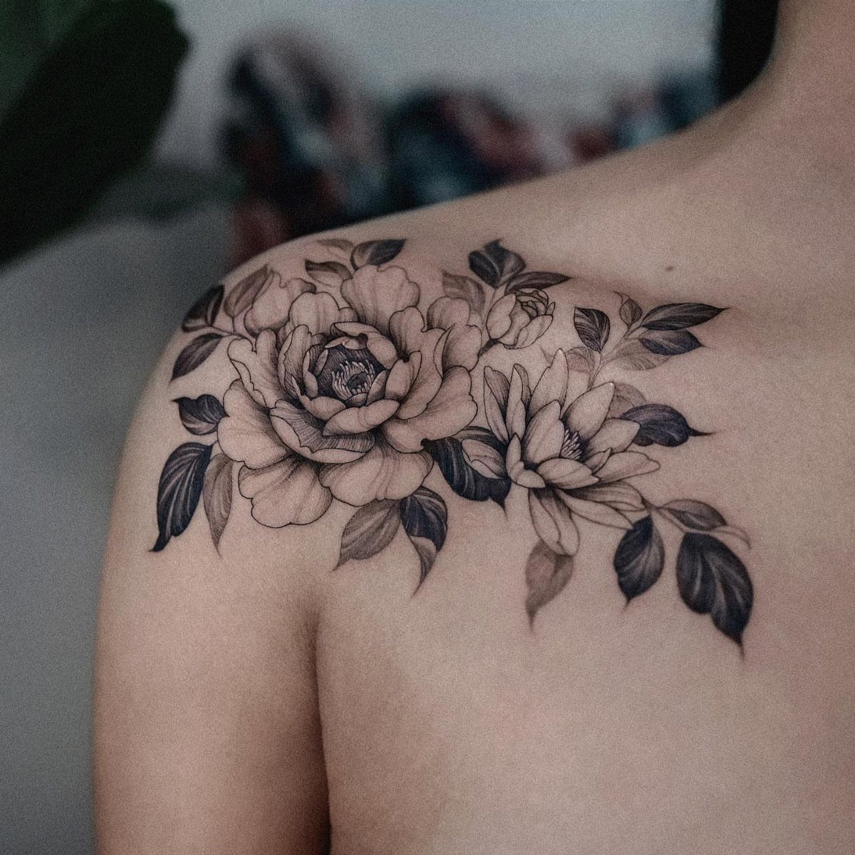 Black and gray tattoo of a peony and lotus flower on a shoulder.