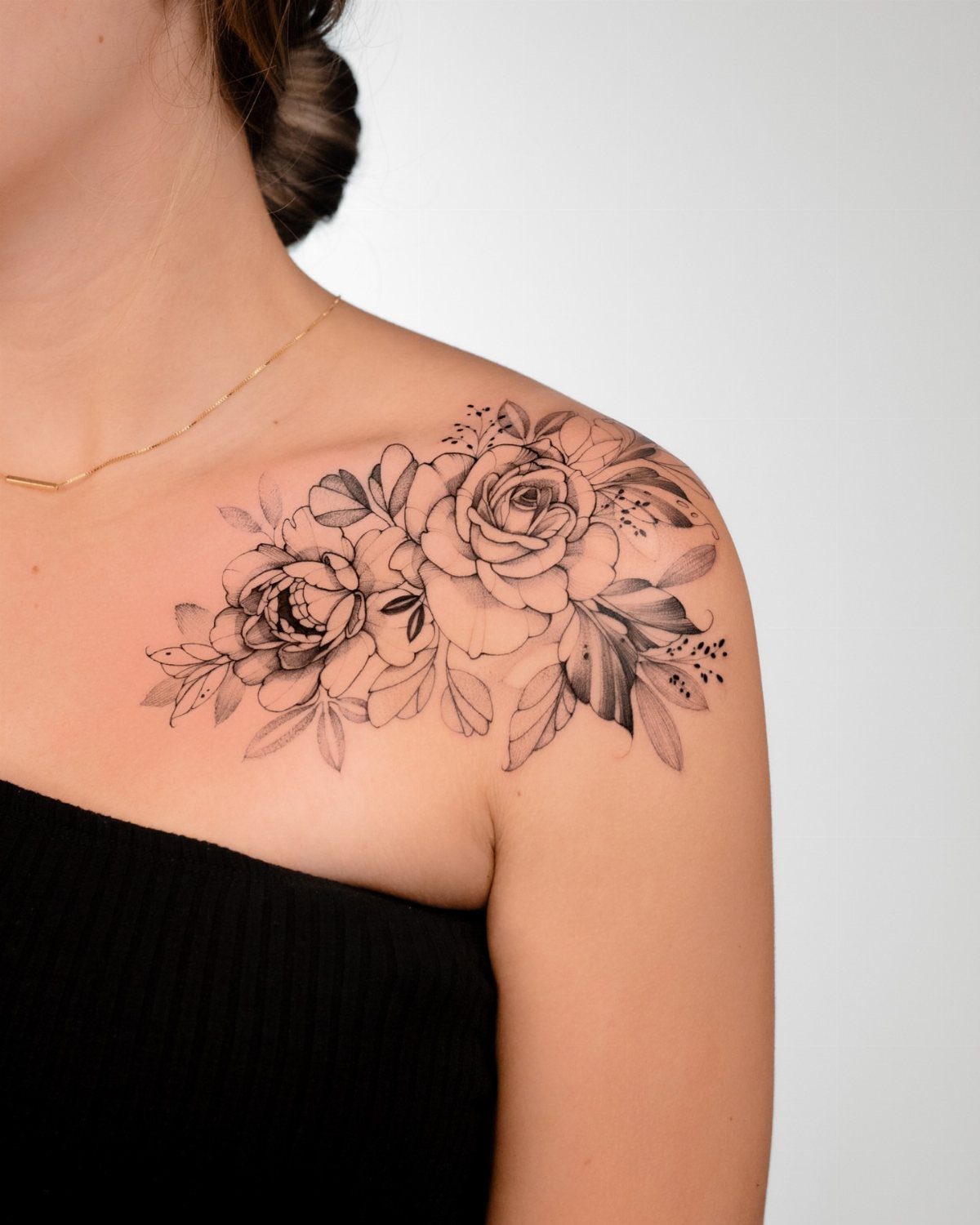 Black and gray peony and rose tattoo on a woman's shoulder and collarbone.
