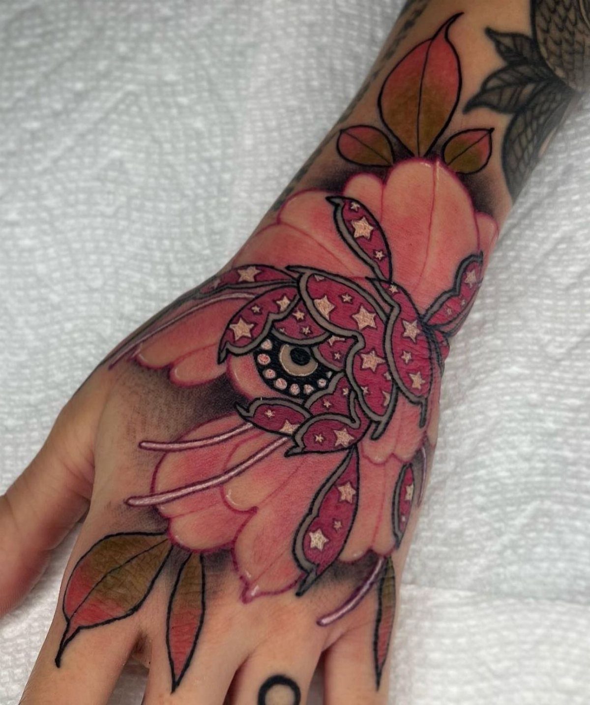 Pink peony flower tattoo on a hand with small stars inside the petals.