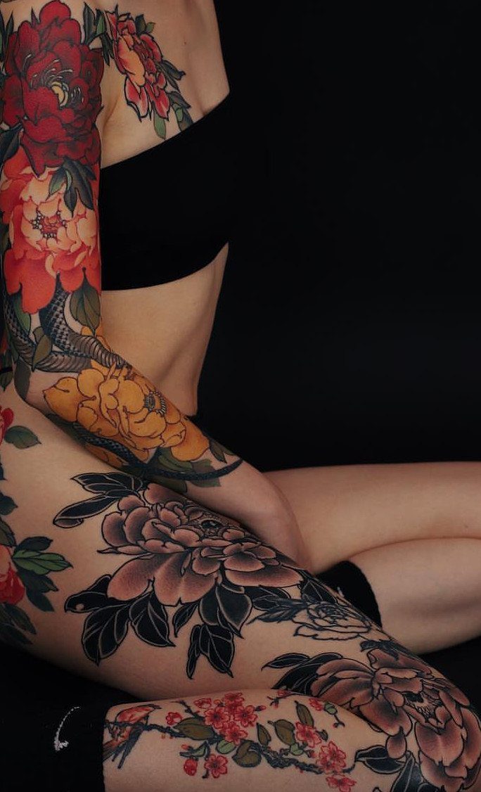 Colorful peony and dragon tattoos on a person's arm and leg against black background