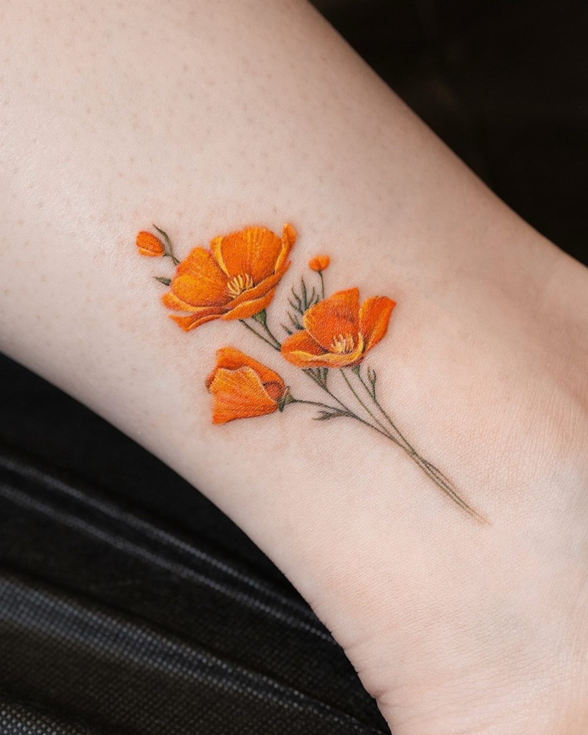Orange poppy flower tattoo with detailed petals and stems on pale skin