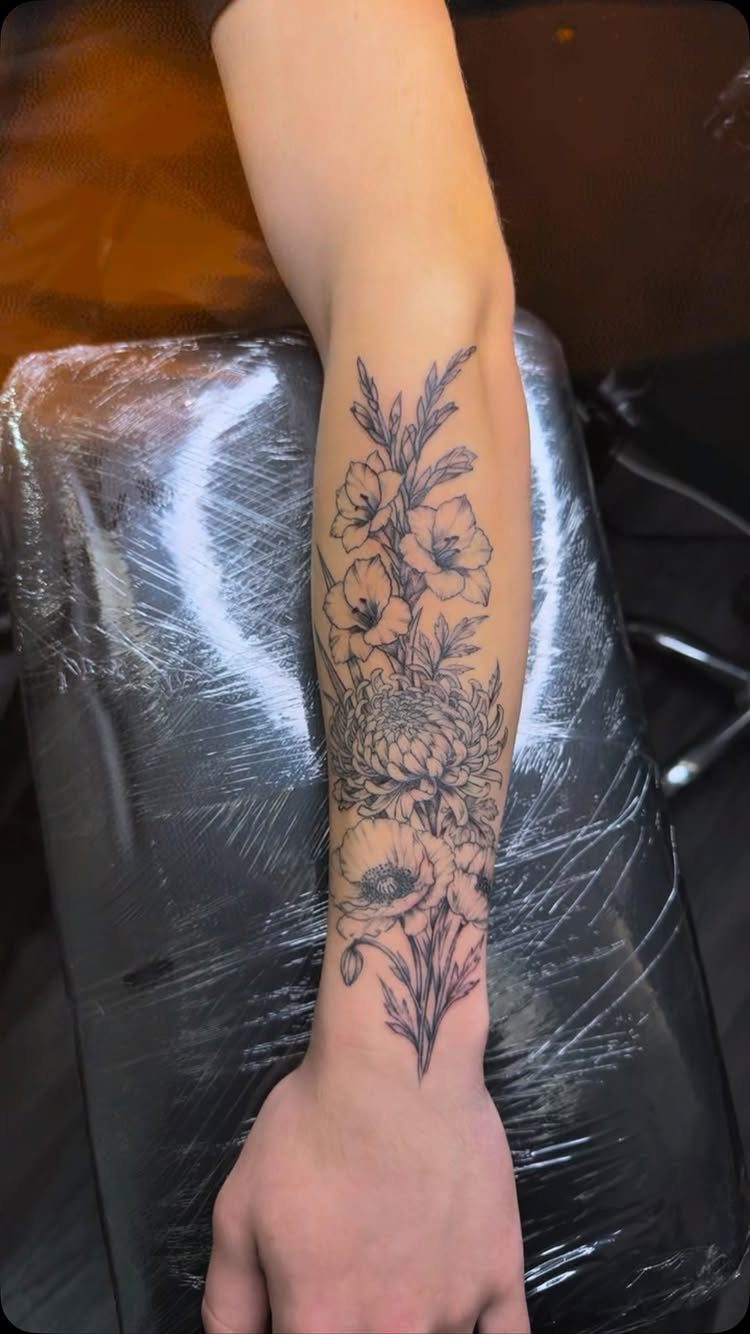 Floral tattoo on a forearm featuring poppies and gladiolus in black ink.