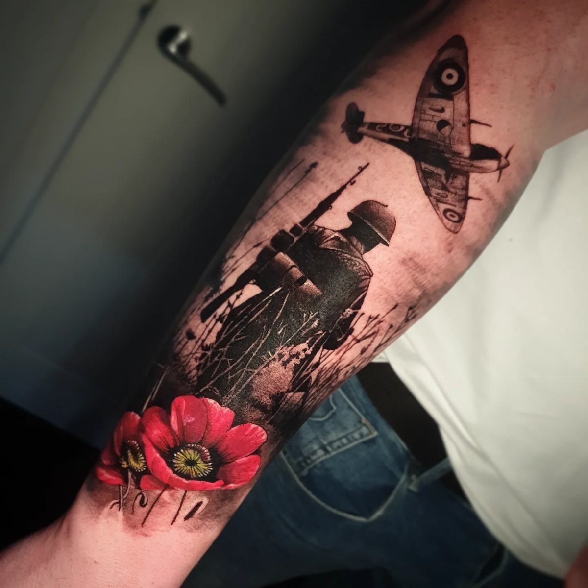 Red poppy flower tattoo with a soldier silhouette and vintage fighter plane on forearm