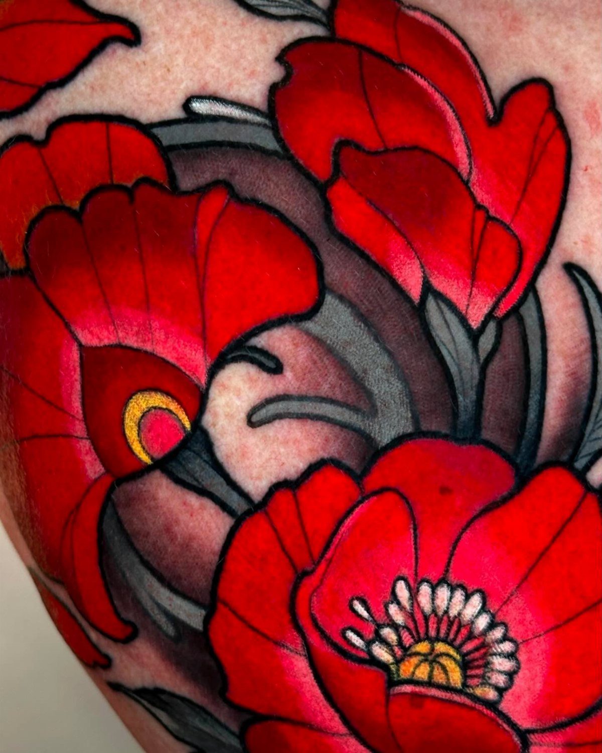 Red poppy flower tattoo with bold black outlines and grey leaves on skin.