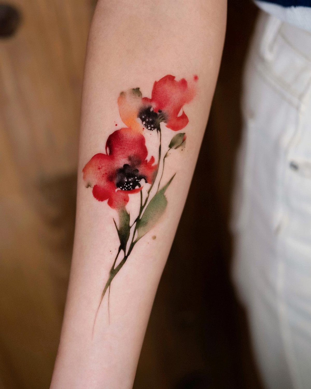 Red poppy flower tattoo in watercolor style on a person's forearm