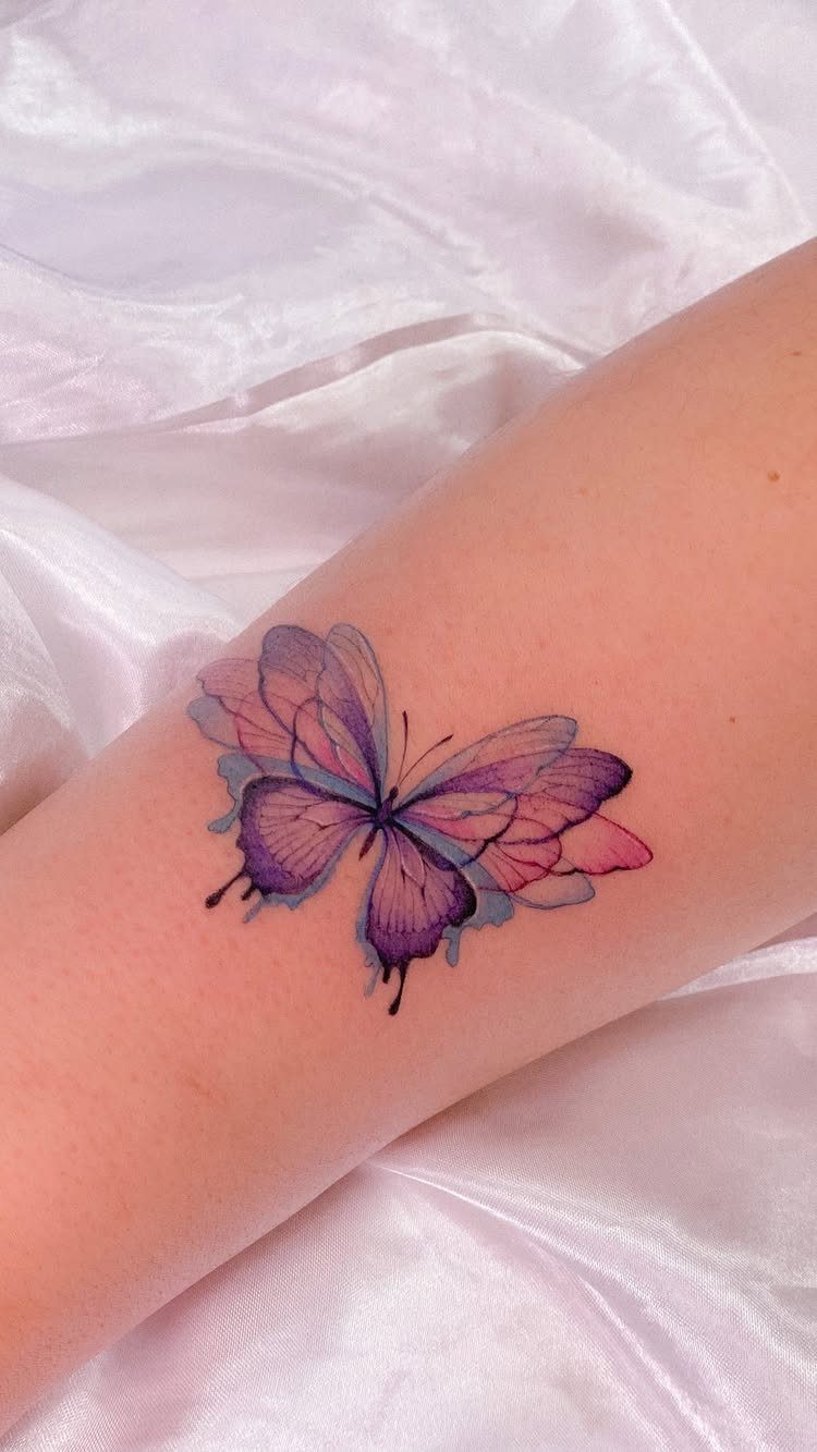 Purple and pink butterfly tattoo on a forearm against white satin fabric