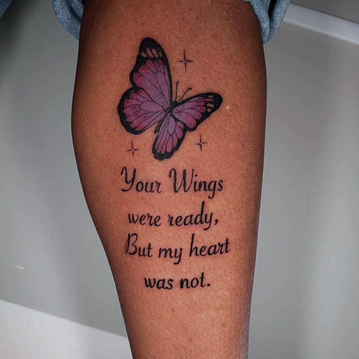 Purple butterfly tattoo with memorial quote on a person's leg