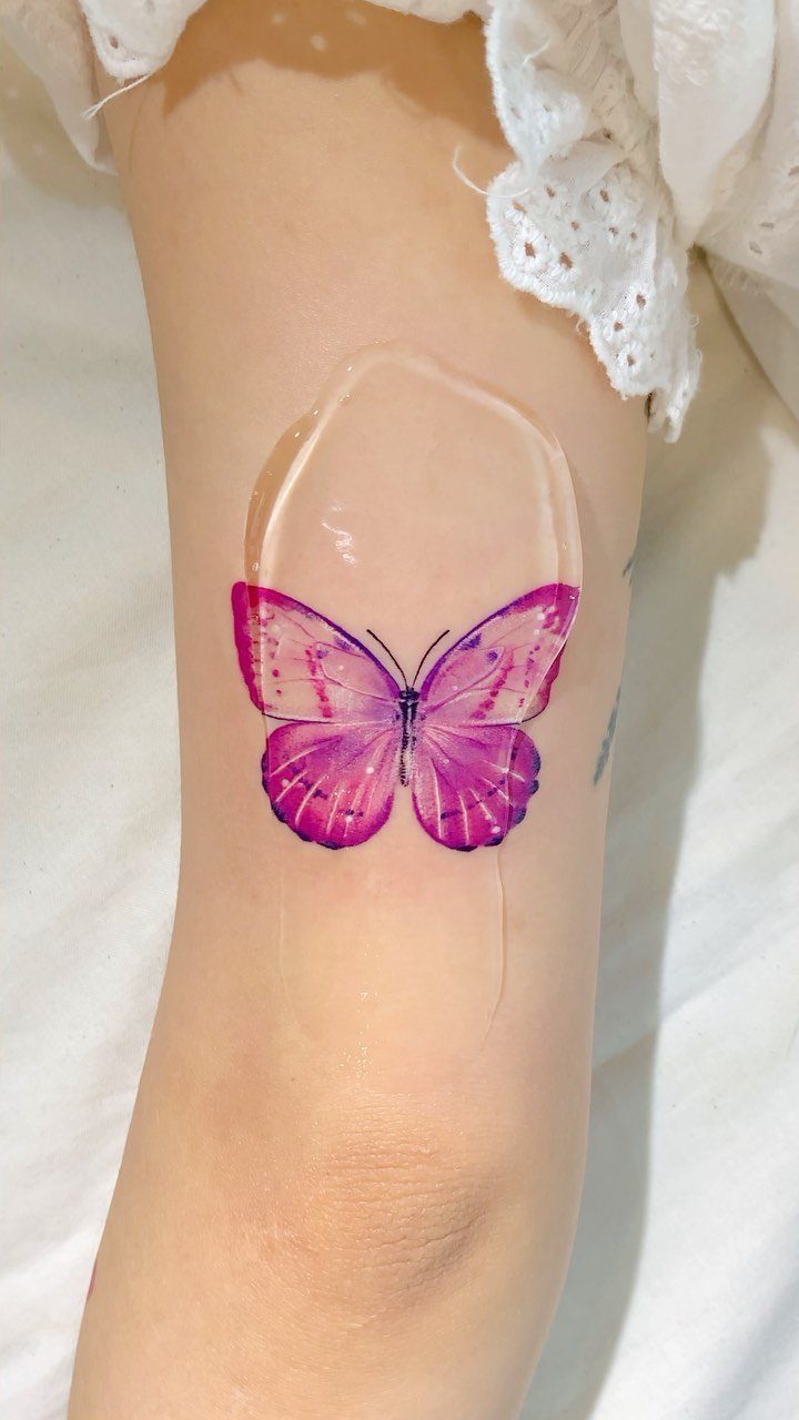 Pink and purple butterfly tattoo on a leg covered by a clear bandage