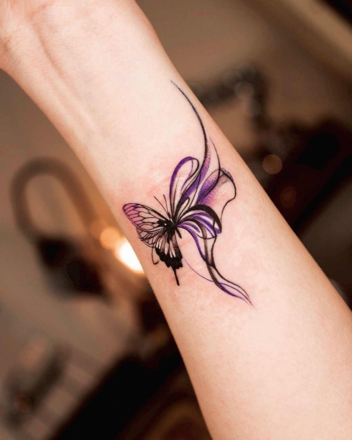 Purple and black butterfly tattoo on a wrist with flowing abstract purple swirls.