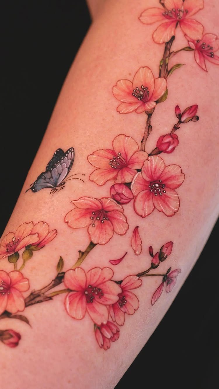 Purple butterfly and pink cherry blossoms tattoo on a person's forearm