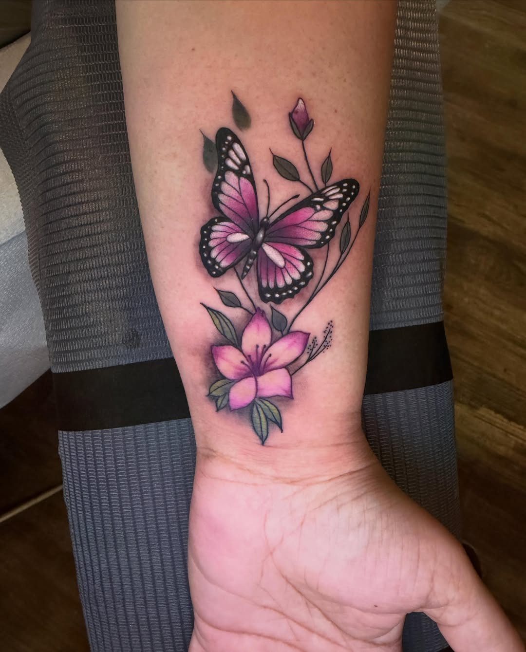 Purple and pink butterfly tattoo with a lily flower on a forearm