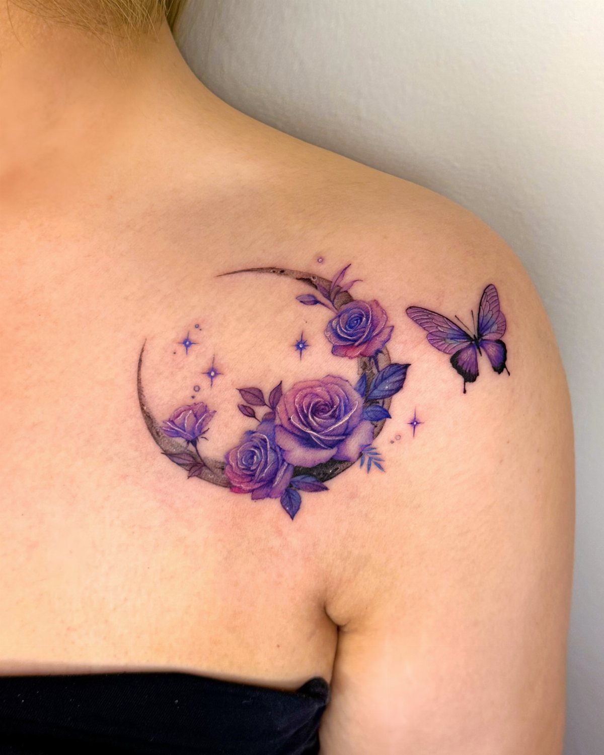 Purple butterfly tattoo next to a crescent moon with purple roses on a shoulder