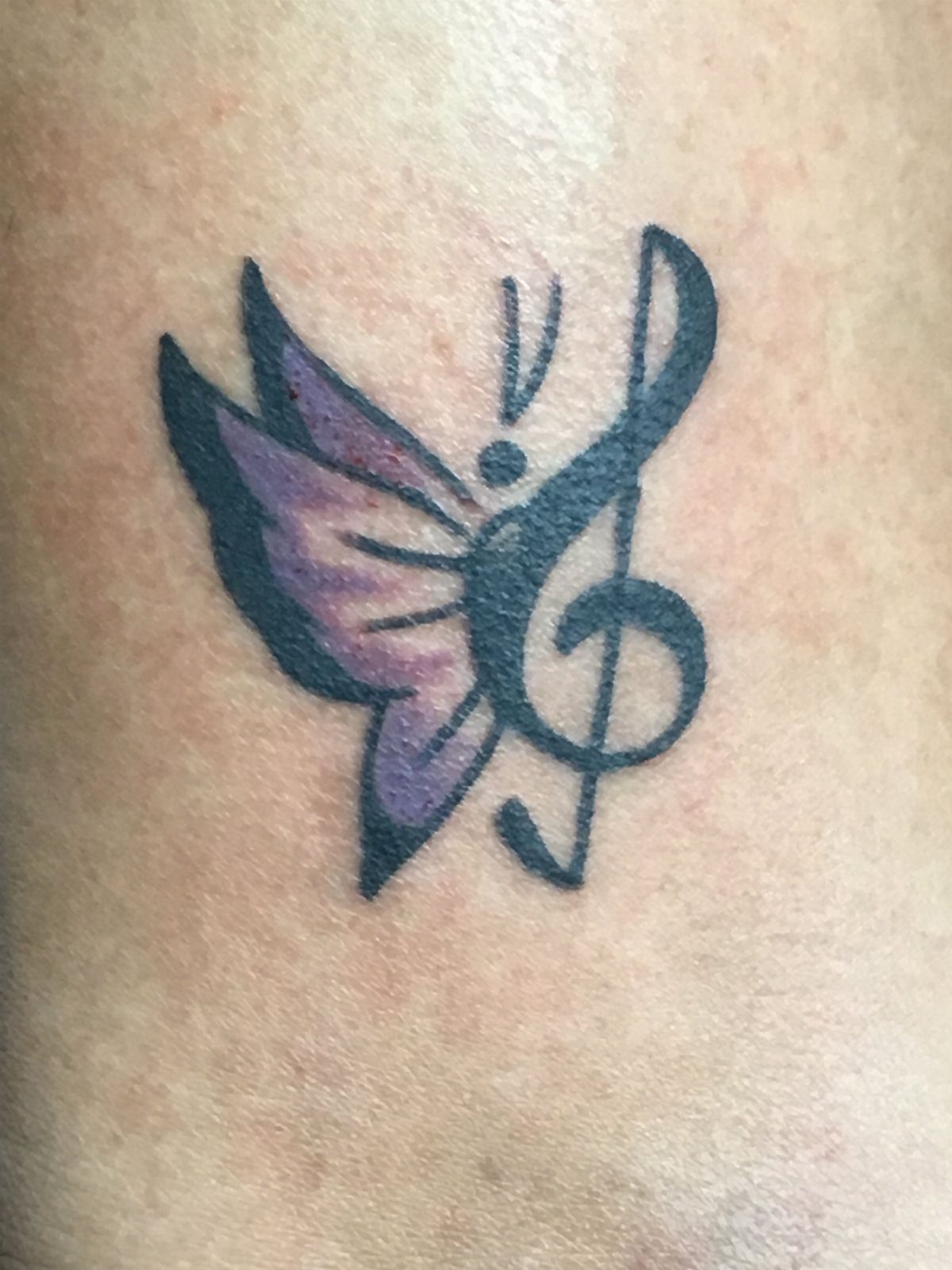 Purple butterfly tattoo with one wing shaped like a black musical G-clef symbol