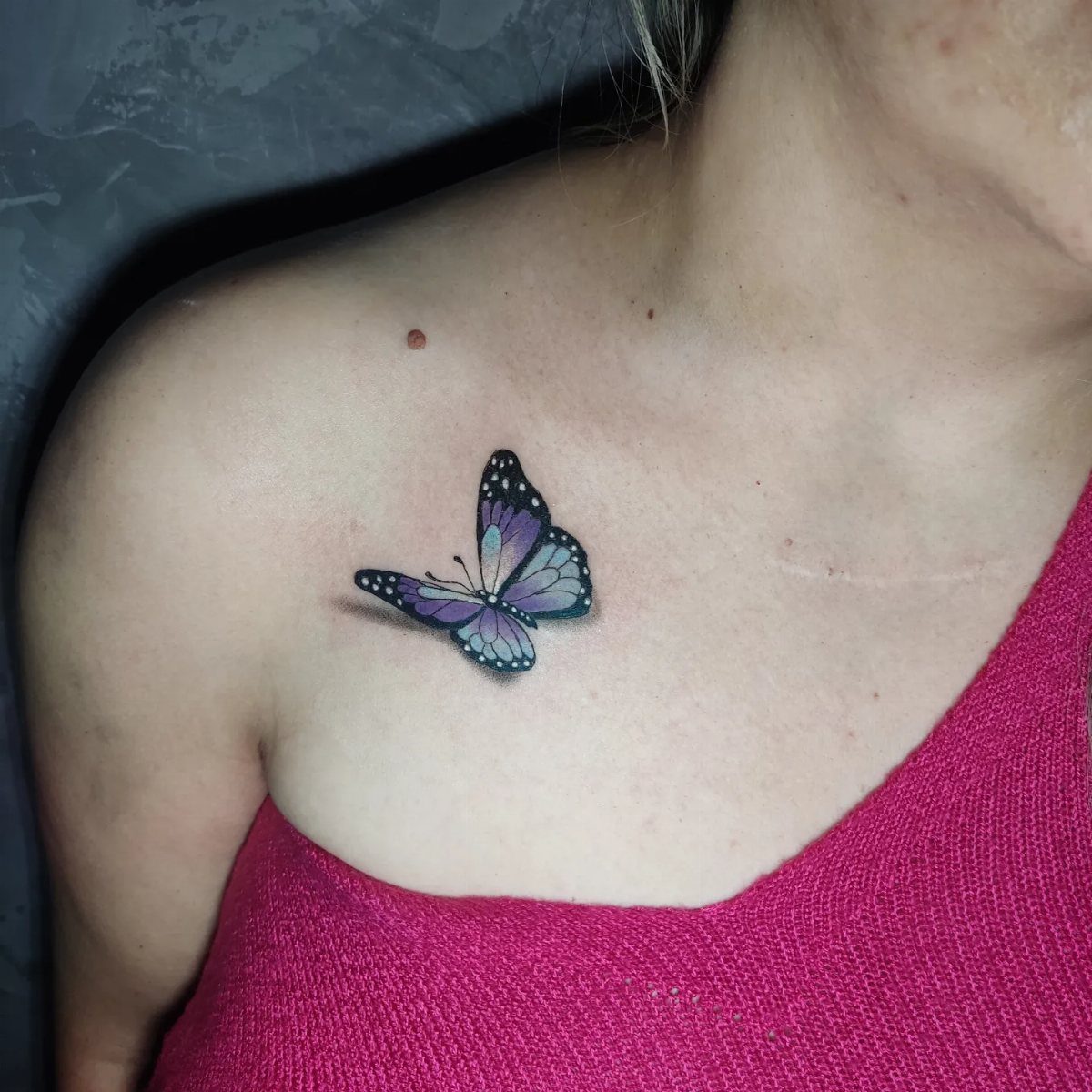 Purple and blue butterfly tattoo on a person's upper chest near the clavicle