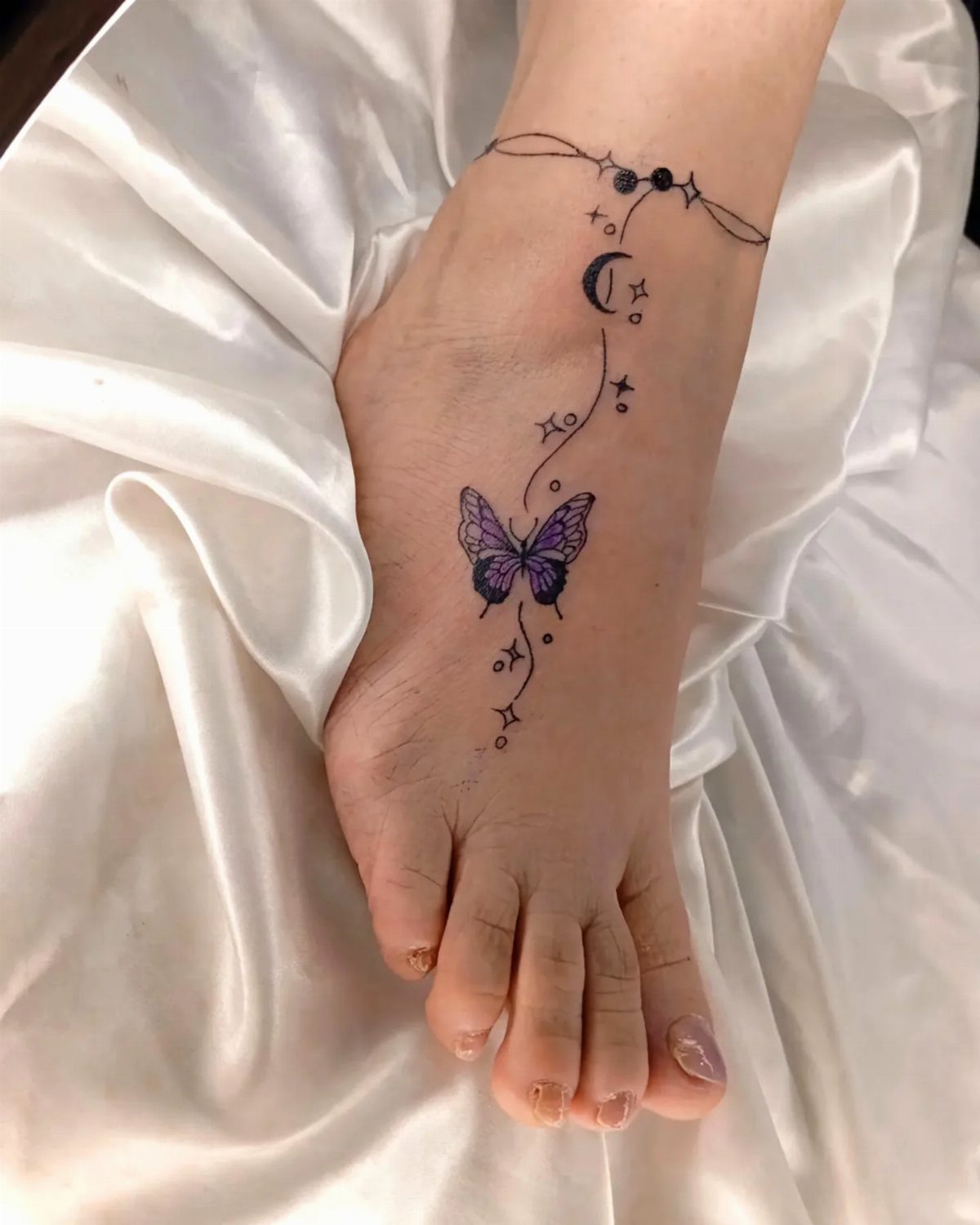Purple butterfly tattoo on the top of a foot with moon and stars.