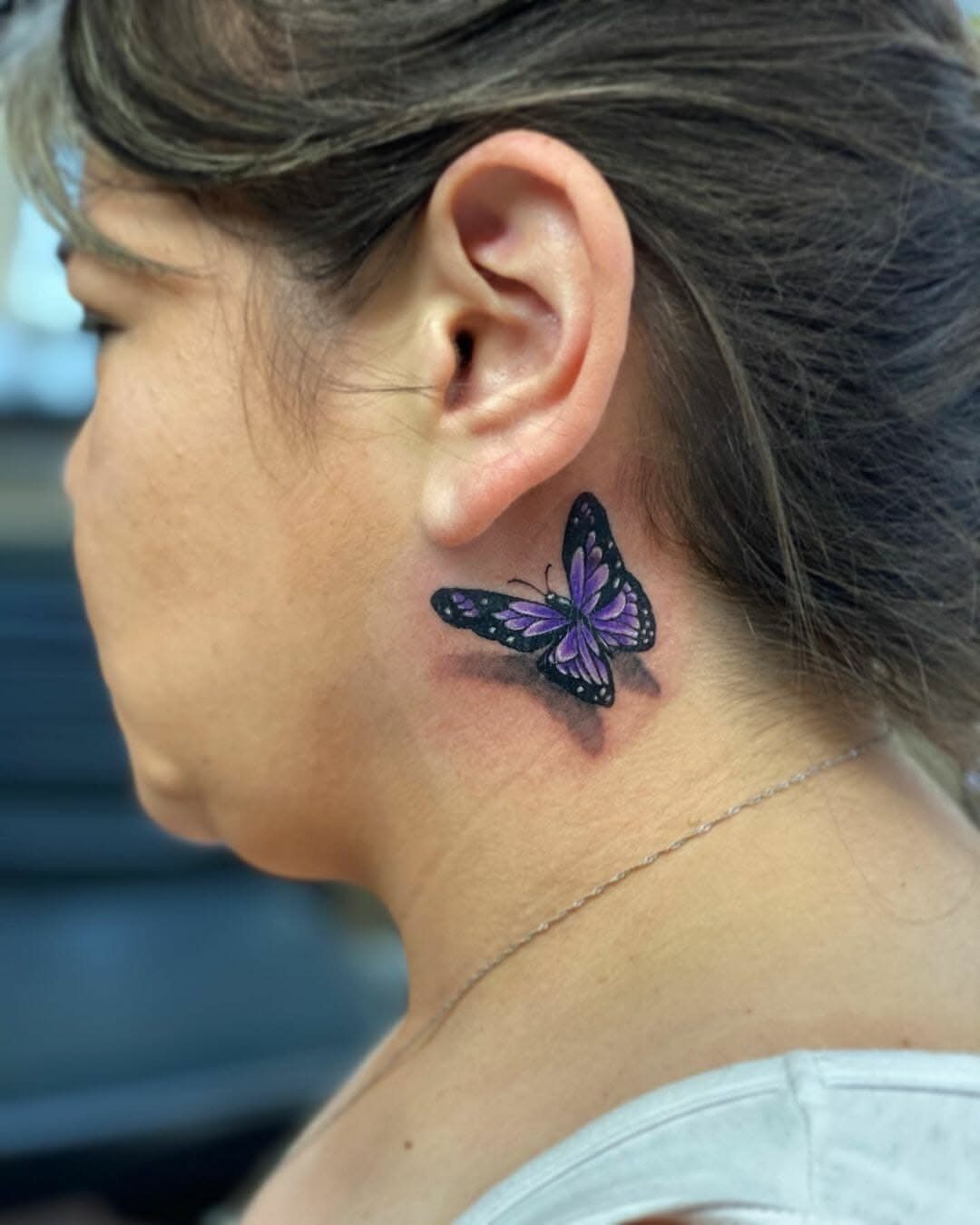 Purple butterfly tattoo with black outlines on the side of a person's neck.