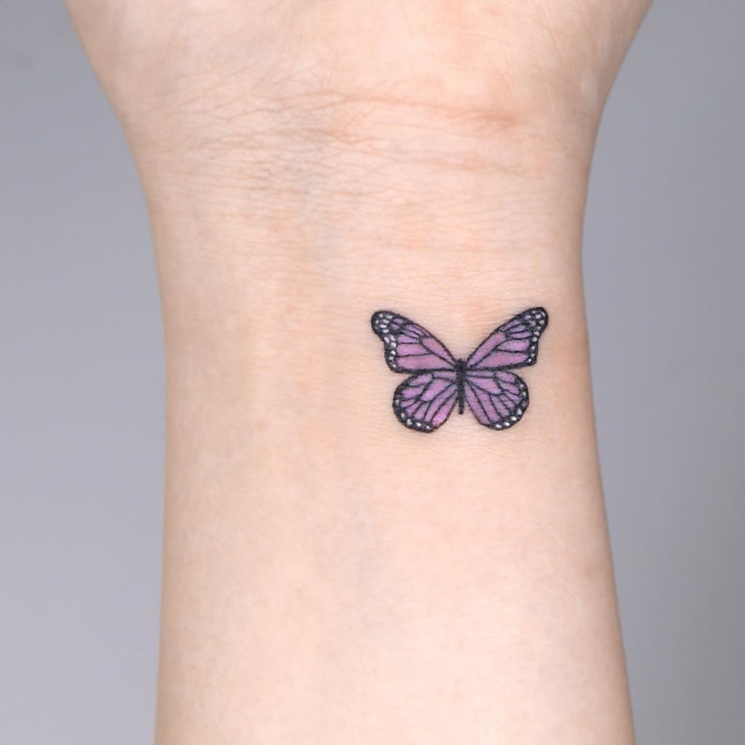Purple butterfly tattoo with black outlines on a person's inner wrist