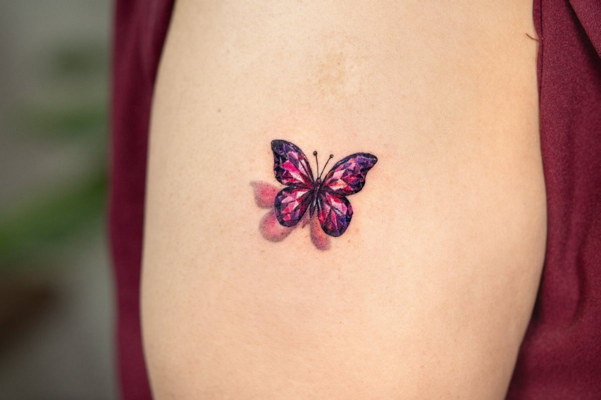 Realistic purple and pink butterfly tattoo with 3D shadow on an upper arm