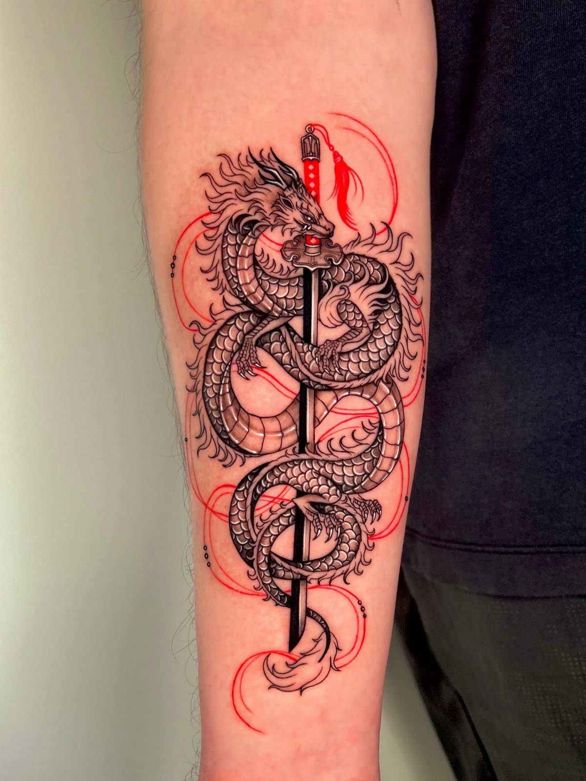 Black and grey dragon tattoo coiled around a sword with red accent lines.