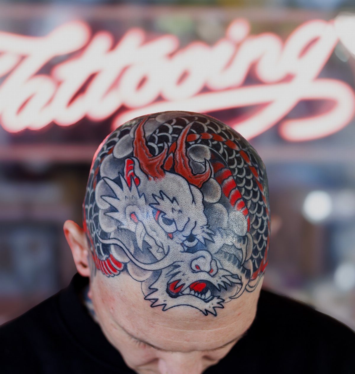 Dragon head tattoo on a bald man's head with red and grey ink.