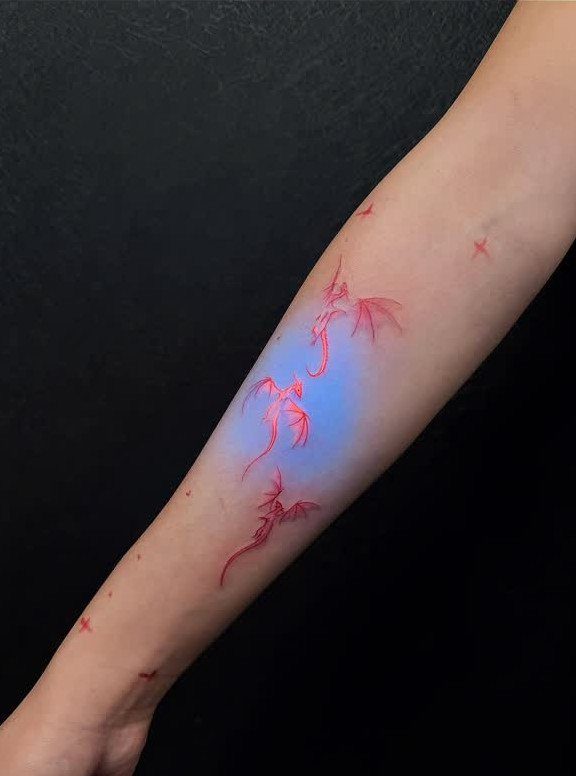 Three small red dragon tattoos on a person's forearm against a black background.