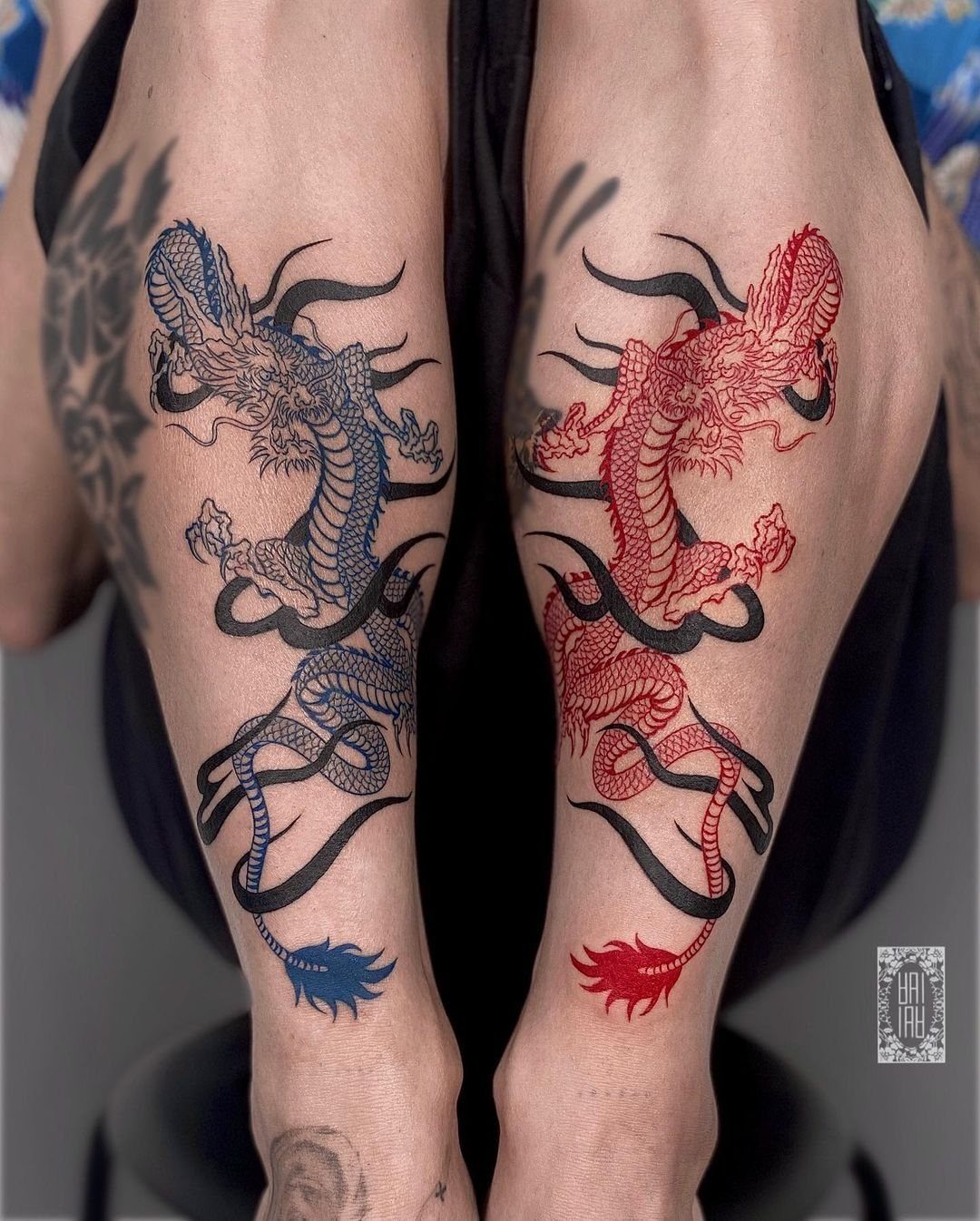 Matching blue and red dragon tattoos on a person's thighs with black outlines.