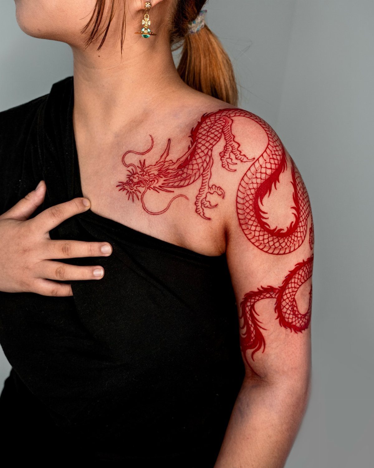 Red dragon tattoo on a woman's shoulder and chest against a grey background