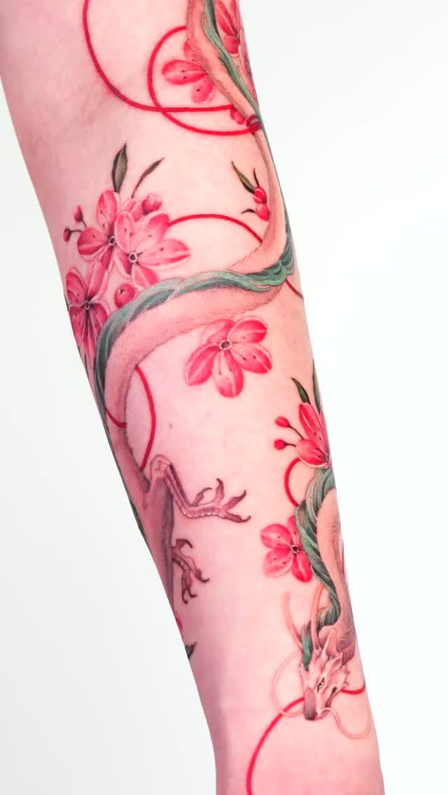 Red dragon tattoo entwined with pink cherry blossoms on a person's arm.