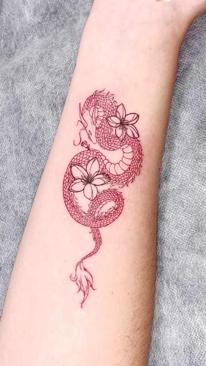 Red dragon tattoo entwined with white lily flowers on a person's forearm
