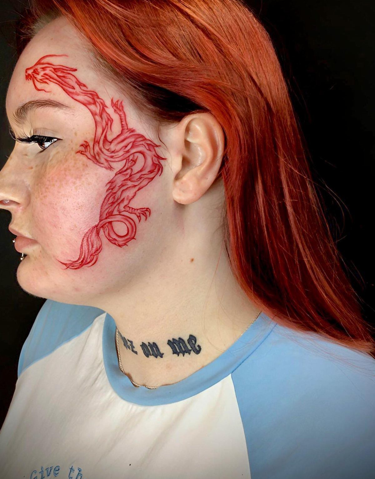 Woman with red hair and a red dragon tattoo on her cheek.