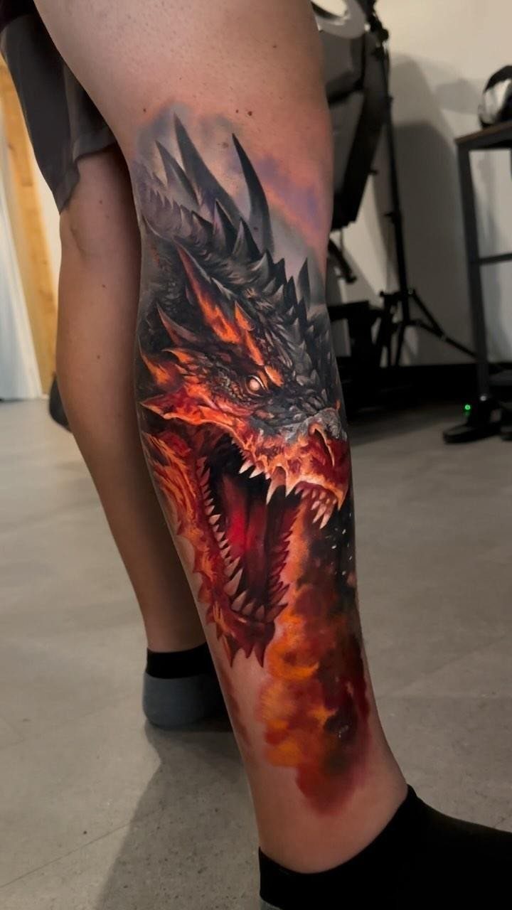 Red dragon head tattoo with open mouth and flames on a lower leg