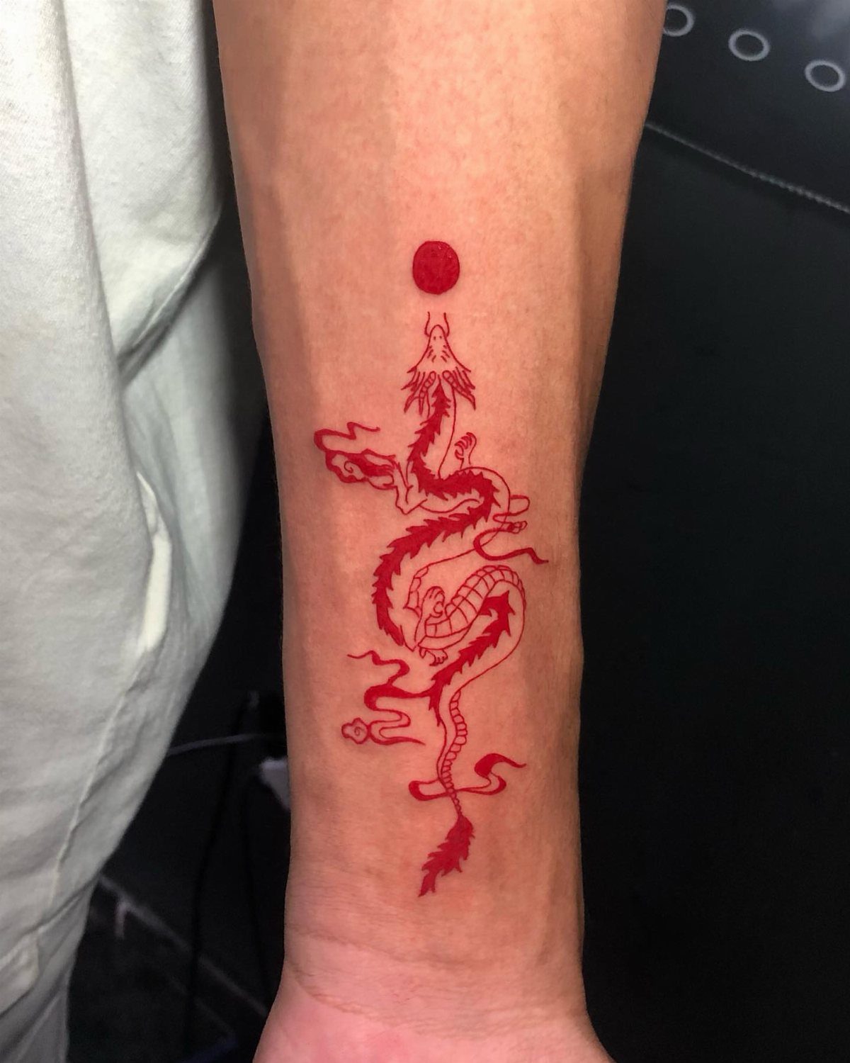 Red Chinese dragon tattoo with a red sun on a person's forearm.