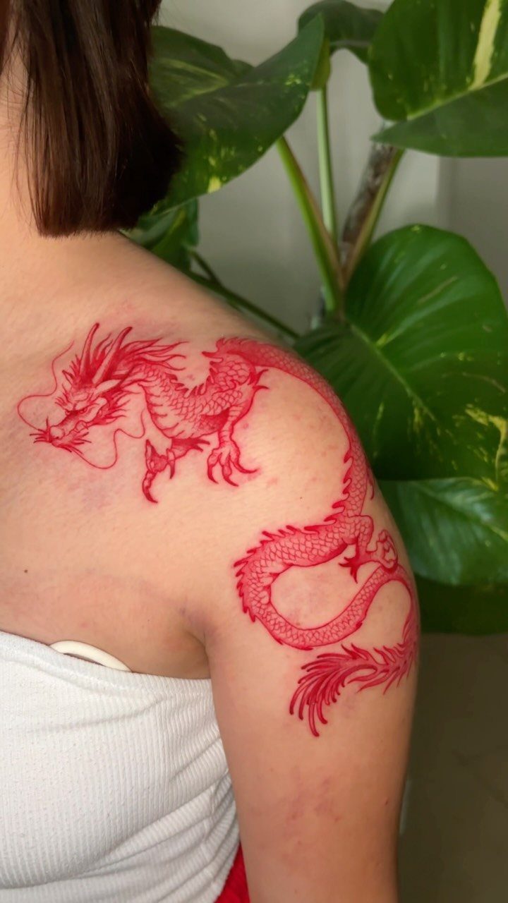 Red dragon tattoo on a person's shoulder and upper back with green leaves.