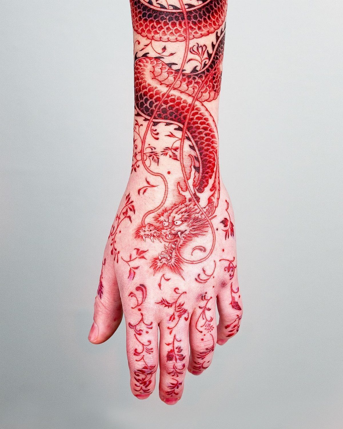 Red Chinese dragon tattoo winding down an arm and across the back of a hand.