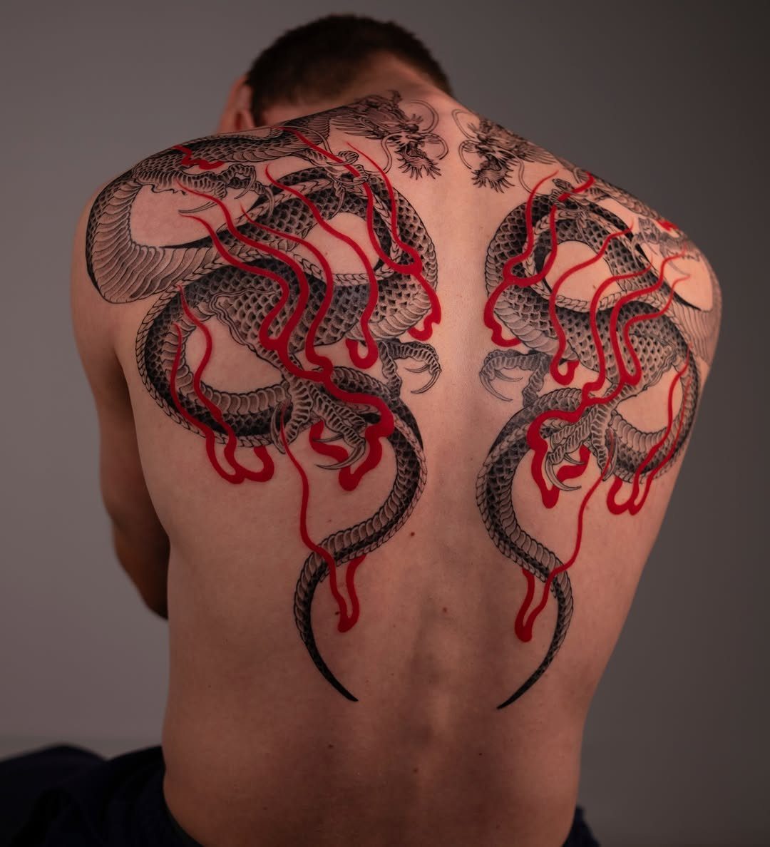 Symmetrical black and red dragon tattoos covering a man's upper back and shoulders.