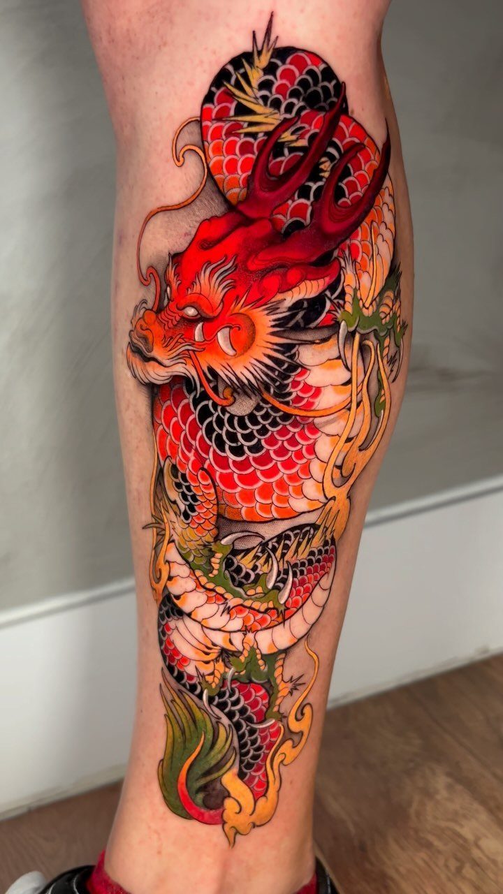 Red dragon tattoo with orange and green details on a person's lower leg