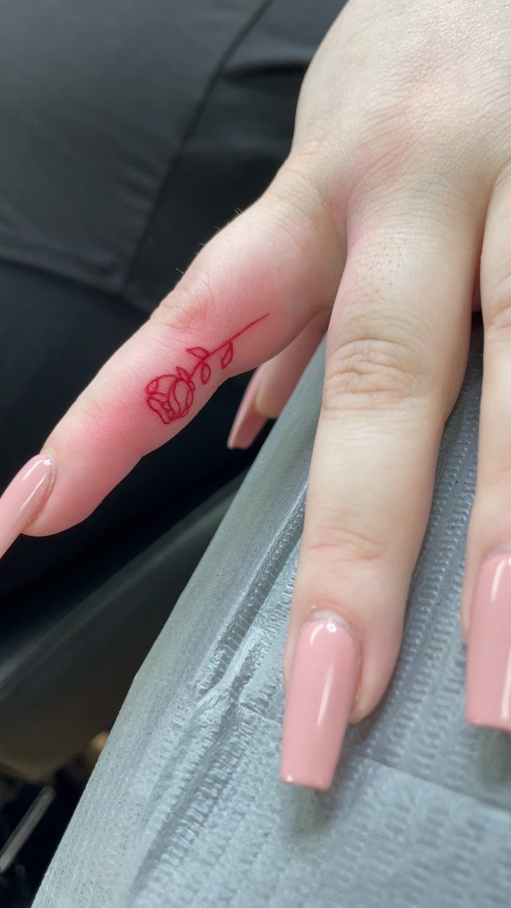 Minimal red rose tattoo on the side of a finger with pink nails