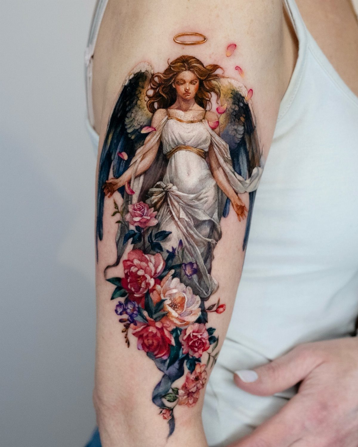 Angel tattoo with dark wings and red roses on a person's upper arm
