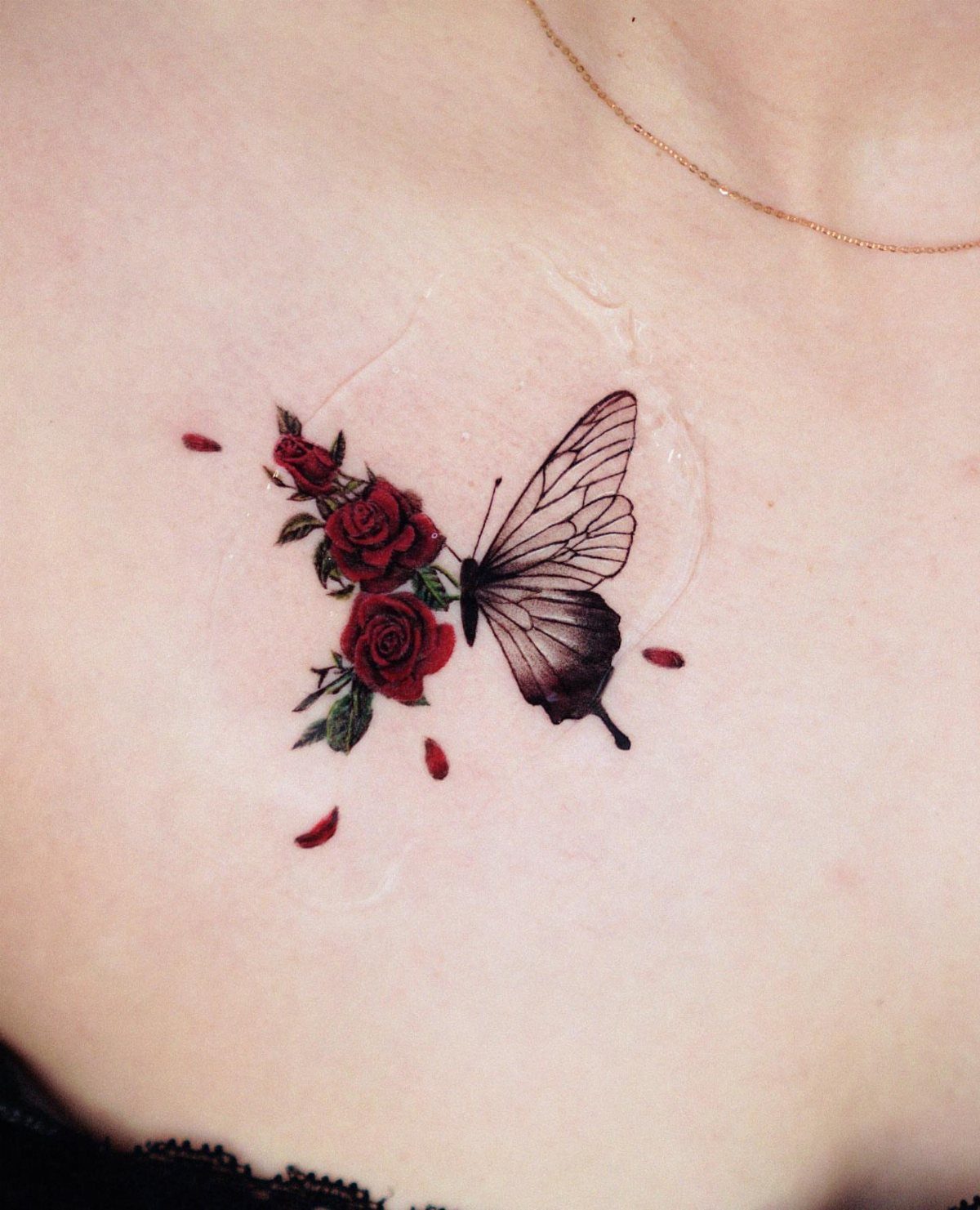 Red rose and butterfly tattoo with floating petals on fair skin