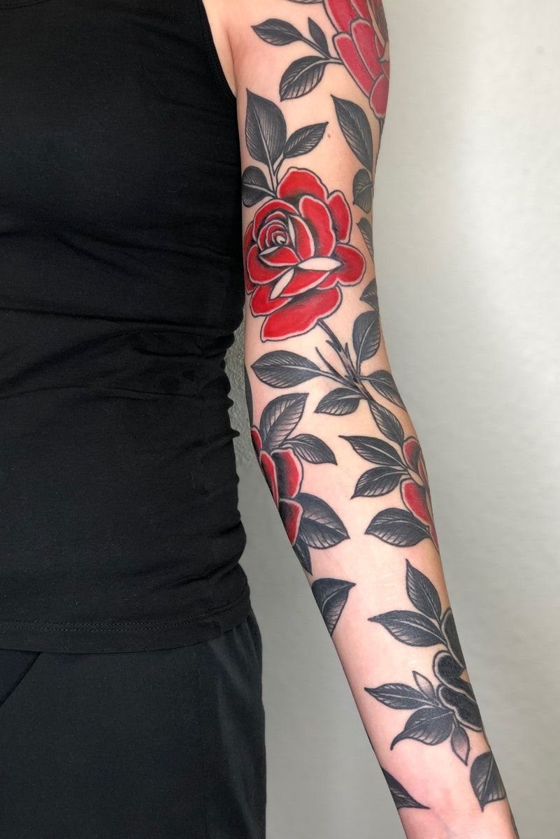 Red rose sleeve tattoo with dark leaves covering a person's entire arm.