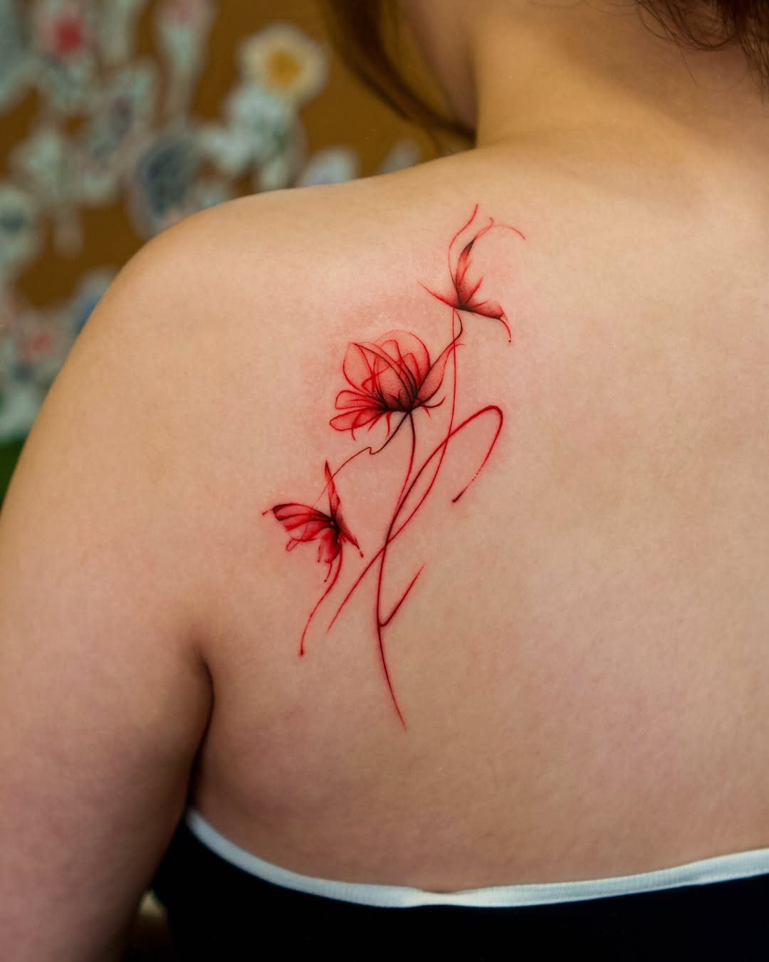 Red rose tattoo with flowing lines on a person's upper back and shoulder