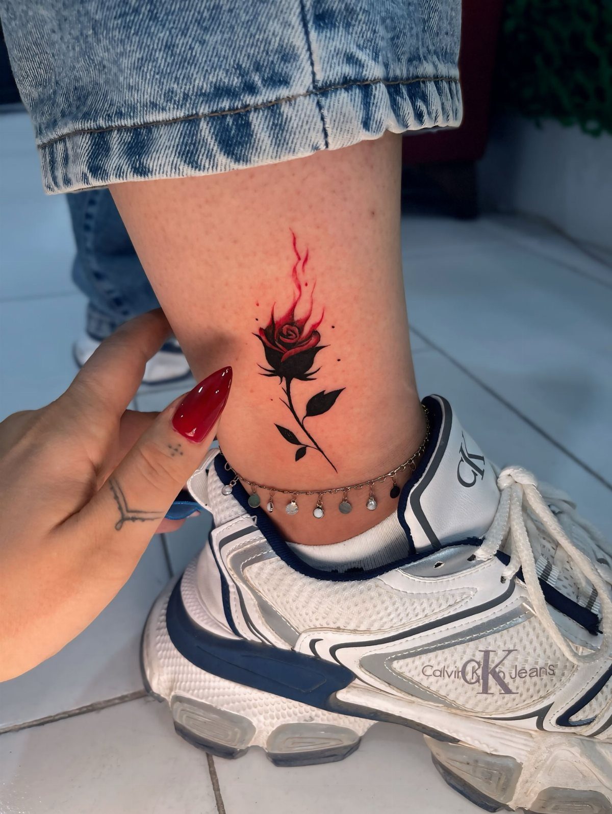 Red rose tattoo with subtle red flames on a person's ankle