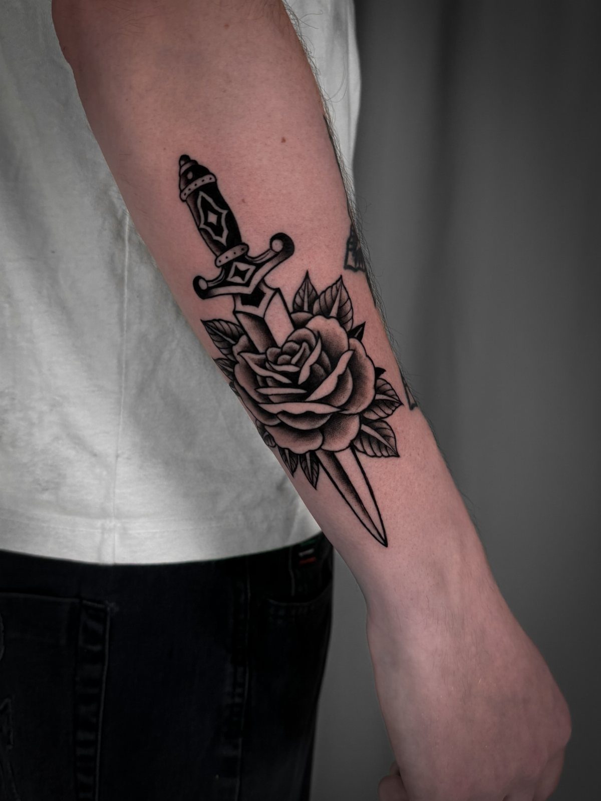 Rose and dagger tattoo in black ink on a person's forearm
