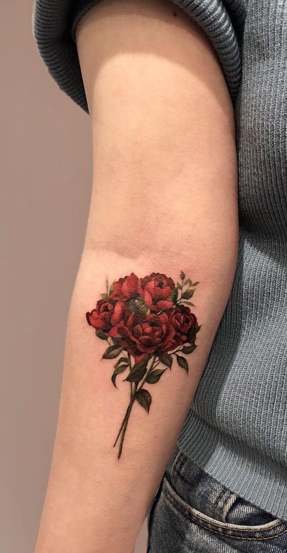 Bouquet of red roses tattoo with green leaves on a person's forearm